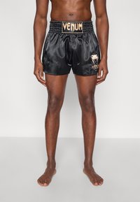 Juodi satino bokso šortai su elastine juosmens juosta ir Venum logotipu. Išskirtos aukso spalvos detalės, aptempto fasono, iki vidurio šlaunies ilgio.