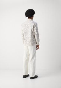 Camisa de manga larga con diseño estampado en color crema y un patrón de paisley azul, combinada con pantalones de pierna ancha blancos y zapatos negros.