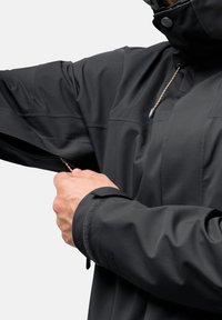 Giacca impermeabile nera con cappuccio, dotata di tasca con zip. Il tessuto testurizzato e i polsini regolabili migliorano la funzionalità.