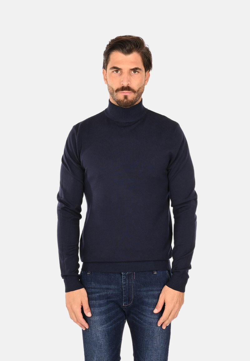 Maglione dolcevita blu navy in materiale lavorato a maglia, con polsini e orlo a coste, abbinato a jeans blu scuro.