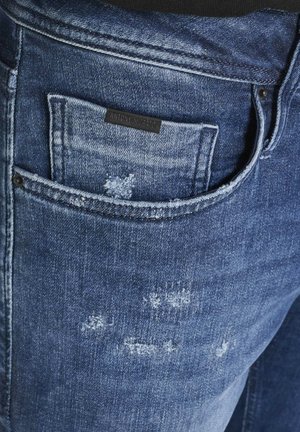 Jeans in denim blu scuro con una texture consumata, dotati di una piccola tasca con un'etichetta nera e cuciture a vista sulla vita.