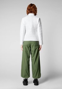 Giacca bianca trapuntata con colletto alto e design testurizzato, abbinata a pantaloni larghi verde oliva e scarpe nera chunky.