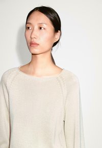 Maglione lavorato a maglia color beige chiaro con scollo rotondo, maniche raglan e finitura texture. Design semplice, tessuto morbido e vestibilità rilassata.