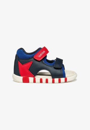 Sandal blu e navy con accento a stella rossa, cinturino regolabile e lati in rete traspirante. Suola testurizzata con strisce bianche e rosse.