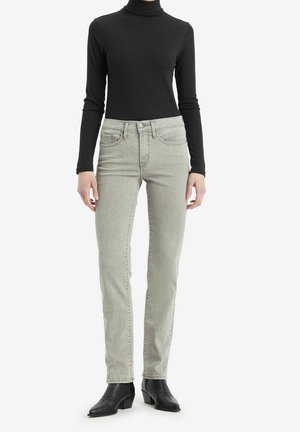 Person wearing light gray slim-fit jeans, black long-sleeve turtleneck, and black ankle boots standing on white background.