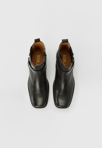 Botas de tobillo de cuero negro con punta cuadrada. Presentan un acabado liso, cremallera lateral y una pequeña pestaña en la parte posterior. El interior es de color marrón claro.