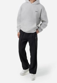 Helles graues, strukturiertes, kapuzenförmiges Fleece-Sweatshirt mit einer Fronttasche; kombiniert mit schwarzen, weit geschnittenen Hosen mit seitlichen Falten und Logo-Details.