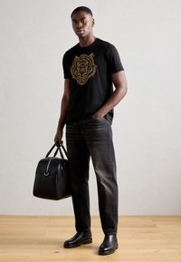 Black t-shirt with gold tiger graphic, gray jeans, black leather boots, and a black duffel bag. Smooth textures and minimalistic design.