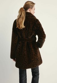 Brązowy płaszcz z futra syntetycznego w leoparda, z paskiem w talii i szerokimi rękawami, noszony na czarnych skórzanych spodniach. Teksturowana i miła w dotyku powierzchnia.