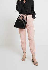 Vaaleanpunaiset cargo-housut, joissa on elastiset lahkeet, yhdistettyinä mustaan pitkähihasaiseen paitaan ja harmaisiin korkeakorkoisiin sandaaleihin. Musta olkalaukku, jossa on hopeisia yksityiskohtia.