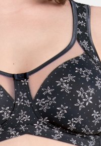 Black bra with floral pattern in white. Soft fabric, mesh accents, adjustable straps, and a front clip closure.
