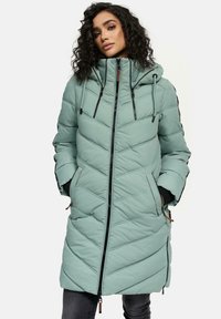 Manteau rembourré vert clair avec un motif en chevrons, capuche ajustable, fermeture éclair et poches latérales. Tissu texturé avec des poignets élastiques.