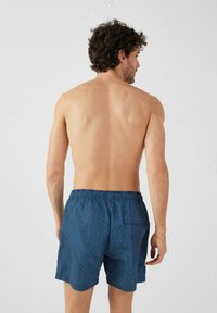 Pantaloni da bagno a righe blu con cintura elastica e tasca posteriore, visti da dietro su una persona con capelli corti e ricci.