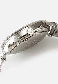 Montre en acier inoxydable avec finition polie, dotée de deux boutons poussoirs, d'une couronne gravée du logo et d'un cadran sombre avec des marquages discrets.