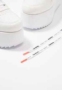 Vita plattformssneakers med en glansig finish, med perforerade detaljer, vita snören och snörändar i orange med varumärkeslogotyp.