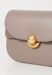 Borsa in pelle grigia con pattina arrotondata, hardware circolare dorato e un morbido accento in suede sul retro. Texture liscia e design minimalista.