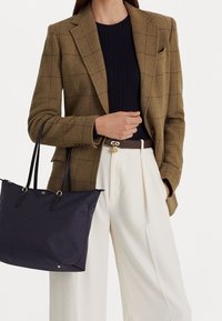 Hnědý kostkovaný blazer, námořnický svetr s vroubkováním, krémové kalhoty a námořnická taška s černými rukojeťmi, zdobená zlatými akcenty a jemnými detaily.