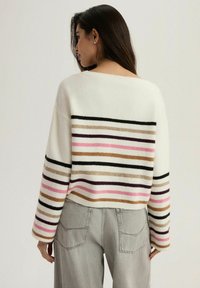 Sweter w paski w kolorze kremowym z poziomymi liniami w różowym, czarnym, brązowym i fioletowym. Miękka dzianina, krótki krój, szerokie rękawy i luźny fason.