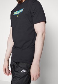 Musta puuvillane T-särk, millel on rinnal värvikas "Lihtsalt tee seda" logo. Lühikesed varrukad, ümmargune kaelus ja laiem lõige.