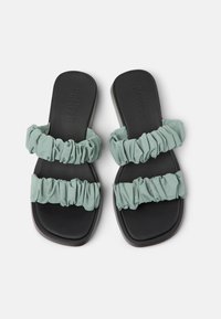 Två slidesandaler med ett rynkat ljusgrönt tygöverdel och en svart gummisula, med en slät, bred remdesign.