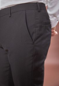 Pantaloni negri cu un design elegant, având o textură fină, pliseuri frontale, buzunare laterale și un buzunar pe spate cu fermoar.