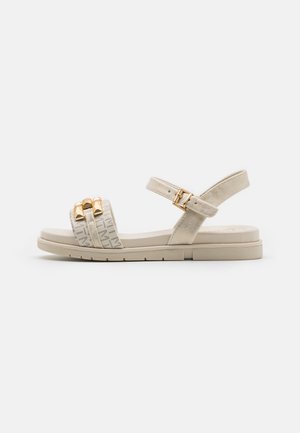 Beige sandals with two textured straps, gold hardware accents, adjustable ankle strap, and a cushioned sole. Flat with minimal tread.