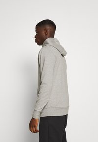 Sudadera gris hecha de tejido de sudadera, con una capucha ajustable, puños acanalados y un corte relajado, vista desde la parte posterior.