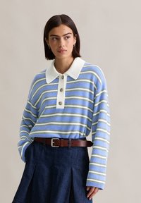 Pasiasty sweter w jasnoniebieskim, zielonym i białym kolorze z białym kołnierzykiem. Posiada trzy guziki i długie rękawy, w połączeniu z ciemnoniebieską spódnicą dżinsową.