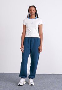 Camiseta blanca de Nike con detalles azules, combinada con pantalones de chándal azul marino que tienen un pequeño logo blanco, llevada con zapatillas deportivas blancas.