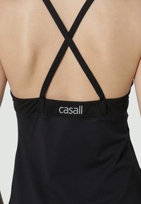 Vue de dos d'une personne portant un haut noir sans manches avec des fines bretelles croisées et le logo "casall" sur le haut du dos.