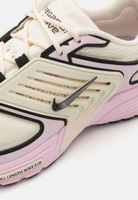 Stilige joggesko med en kremfarget mesh-overdel, rosa detaljer, svarte elementer og en fremtredende svart swoosh-logo på siden.