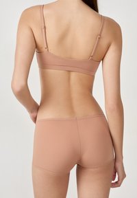 Reggiseno marrone chiaro e short coordinati con texture liscia, spalline regolabili e bordi senza cuciture, visti da dietro.