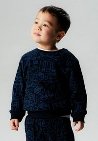 Marineblå genser med lyseblå grafiske motiver som viser ulike objekter, ribbestrikkede mansjetter og rund hals. Egnet for aktiv bruk.