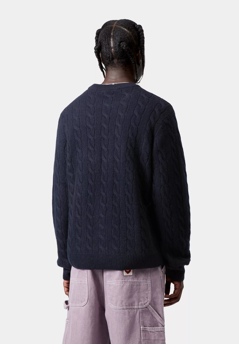 Maglione navy a maglia grossa con texture spessa, scollo rotondo e polsini a coste. Abbinato a pantaloni cargo lilla chiaro con tasche.