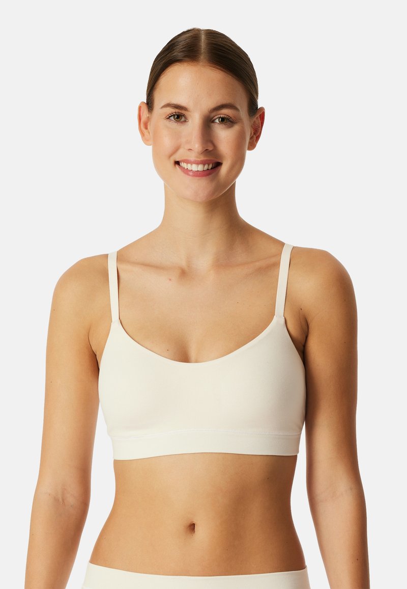 Lyse beige bh med justerbare stropper, sømløst design, blødt stof og rund halsudskæring. Har et bredt underbånd for støtte.