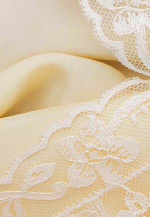 Crème satijnen stof met delicate witte kant met bloem- en bladmotieven langs de randen.