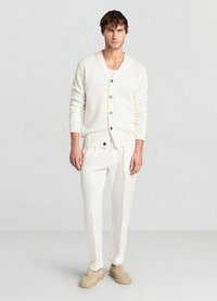 Weißer Strickcardigan mit V-Ausschnitt und drei Knöpfen, getragen über einem weißen T-Shirt und kombiniert mit maßgeschneiderten weißen Hosen und beigen Slippern.