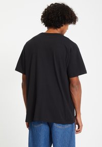 Zwarte katoenen T-shirt met korte mouwen, ronde halslijn en een losse fit, gecombineerd met lichtblauwe jeans. Geen zichtbare patronen of grafische elementen.