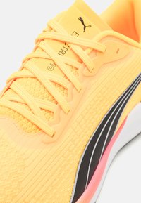 Scarpa da corsa Puma di un vivace giallo, con tessuto a rete testurizzato, strisce nere, lacci e una suola morbida e ammortizzata con accenti rosa.
