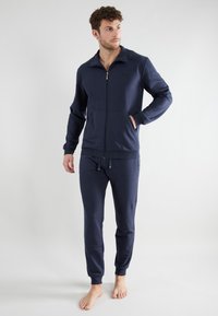Navy blue zip-up jacket with a high collar, featuring front pockets. Paired with matching jogger pants that have elastic cuffs and waistband.