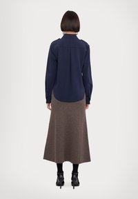 Chemise à manches longues marine avec une fente dans le dos, associée à une jupe maxi côtelée marron, des bottines noires et des collants sombres.