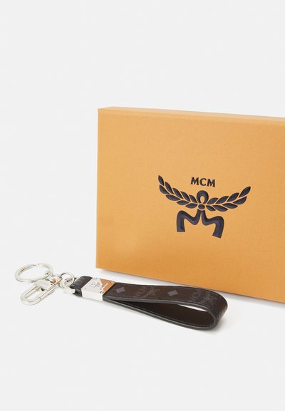 MCM nøkkelring i svart skinn med logo-mønster, utstyrt med sølvfarget hardware og en sirkulær nøkkelring, presentert sammen med en oransje teksturert eske.