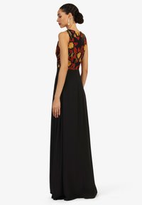 Maxikleid mit einem floralen Oberteil in Rot und Gelb, kombiniert mit einem eleganten schwarzen Rock. Glatter Stoff und ärmelloses Design.