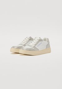 Sneaker bianche e argentate con tomaia in pelle liscia, punta perforata e suola in gomma crema. Presentano lacci piatti e accenti di branding sottili.