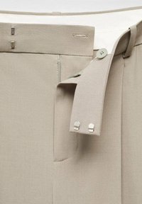Pantalons beiges en tissu lisse, avec une fermeture éclair et un bouton. Comprend des accents métalliques et une taille cintrée avec passants de ceinture.