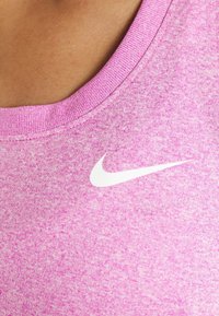 Vaaleanpunainen urheilu-tankkitoppi, jossa on teksturoitu kangas ja pyöreä kaula-aukko. Vasemmalla puolella on valkoinen Nike-logo.