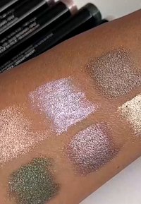 Stalen van metallic oogschaduw op de huid: lichtroze, groen, goud en bruine tinten met glans en verschillende texturen in vierkante vormen.