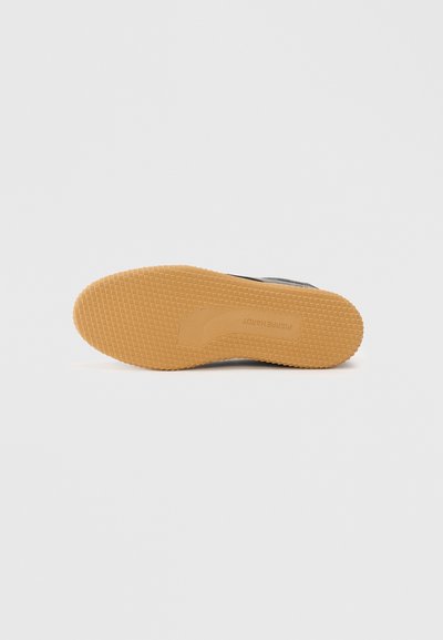 Graue Sneaker mit einer strukturierten Gummiaußensohle und einer braunen Gummisohle. Verfügt über ein gestepptes Obermaterial und ein Branding an der Seite.