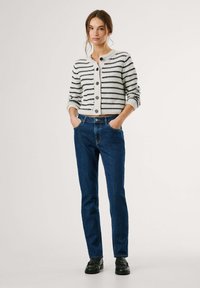 Cardigan lavorato a maglia in bianco con strisce blu navy, caratterizzato da un collo rotondo e cinque bottoni. Abbinato a jeans a gamba dritta blu scuro e scarpe nere.