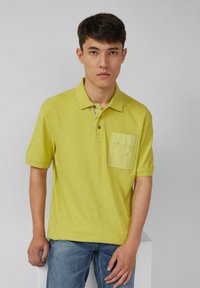 Koszulka polo z krótkim rękawem w jasnym zielonym kolorze, z teksturowanej tkaniny, kołnierzykiem, zapięciem na trzy guziki i przednią kieszonką.